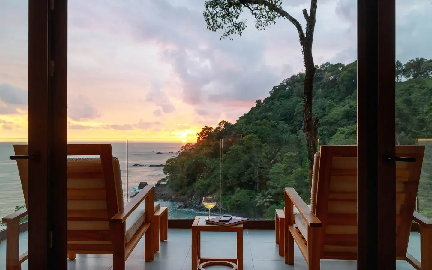 Sunset over the Pacific from the terrace of an Ocean View Premium Suite at Arenas del Mar, Manuel Antonio, two chairs and a glass of wine