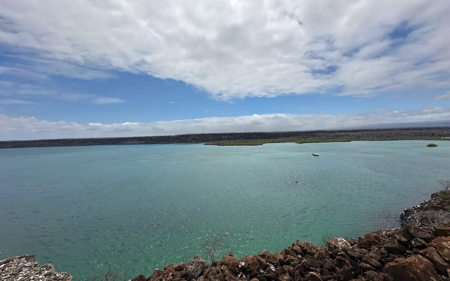 A teal lagoon behind a lava shoreline under a wide cloudy sky on Santa Cruz island, Galápagos