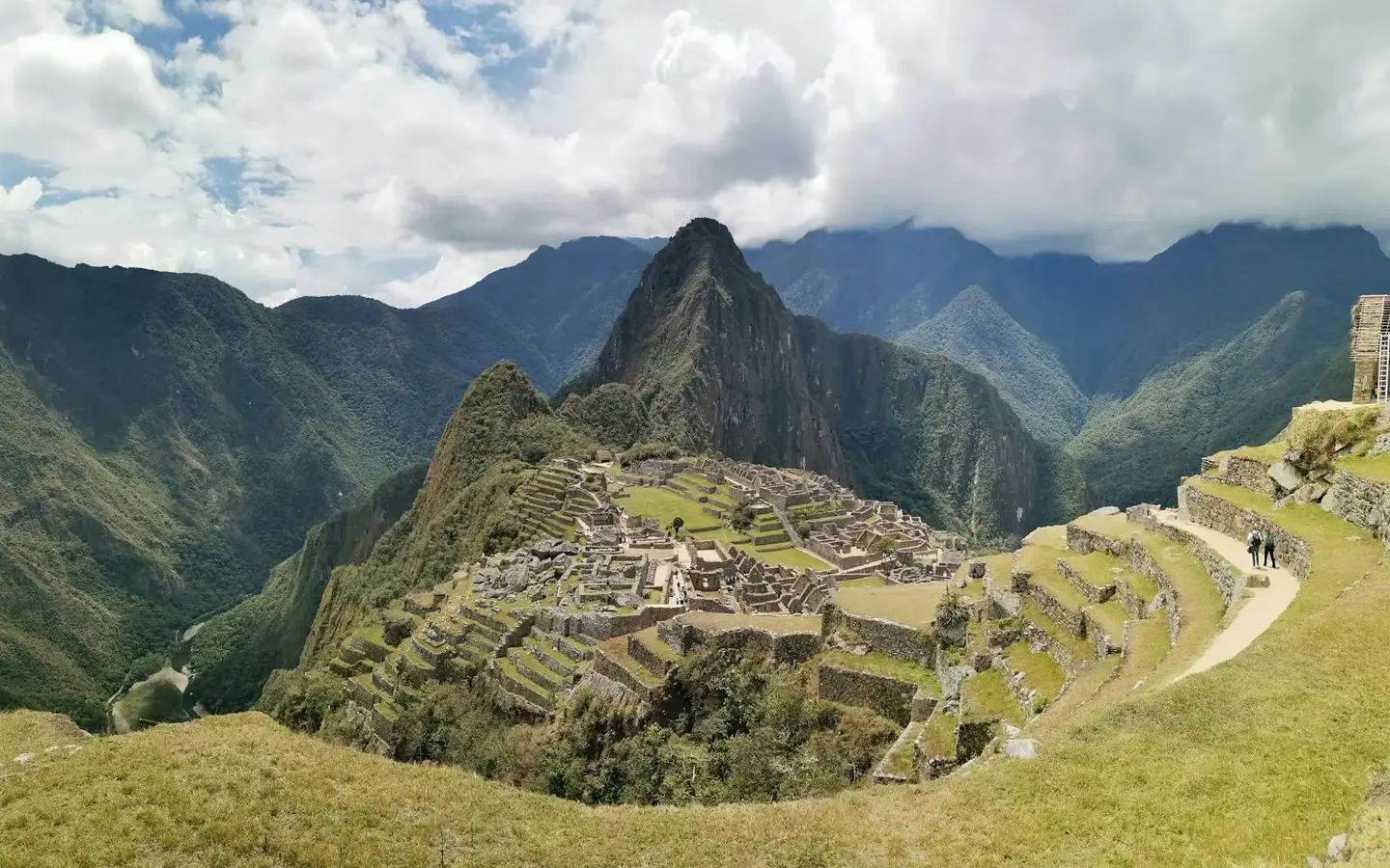 Panoramic view of the ancient Inca citadel of Machu Picchu with Huayna Picchu mountain rising behind, surrounded by lush green Andean peaks