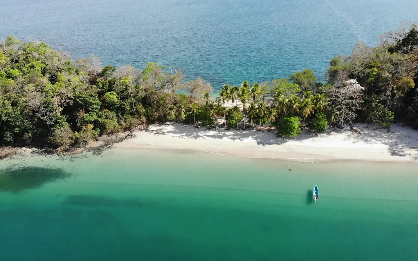 Aerial view of a turquoise cove, white-sand beach and forested island with a small boat, Panama