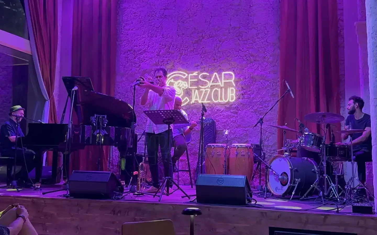 A jazz band performs on a stage under purple lights at Cesar Jazz Club.